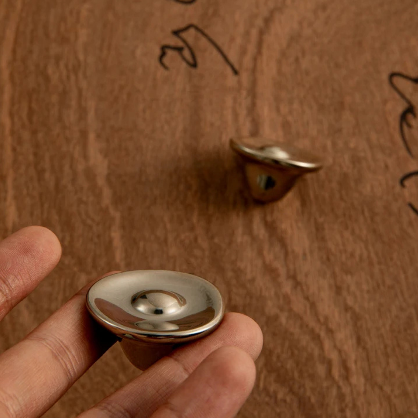 Person holding a shiny round metal cabinet knob with another knob in the background