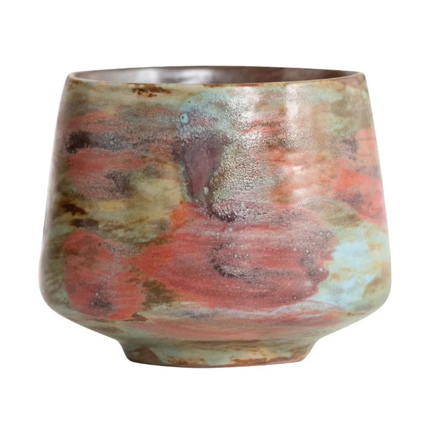 Handmade ceramic cup with textured red, green, and turquoise glaze sitting on a white tabletop.