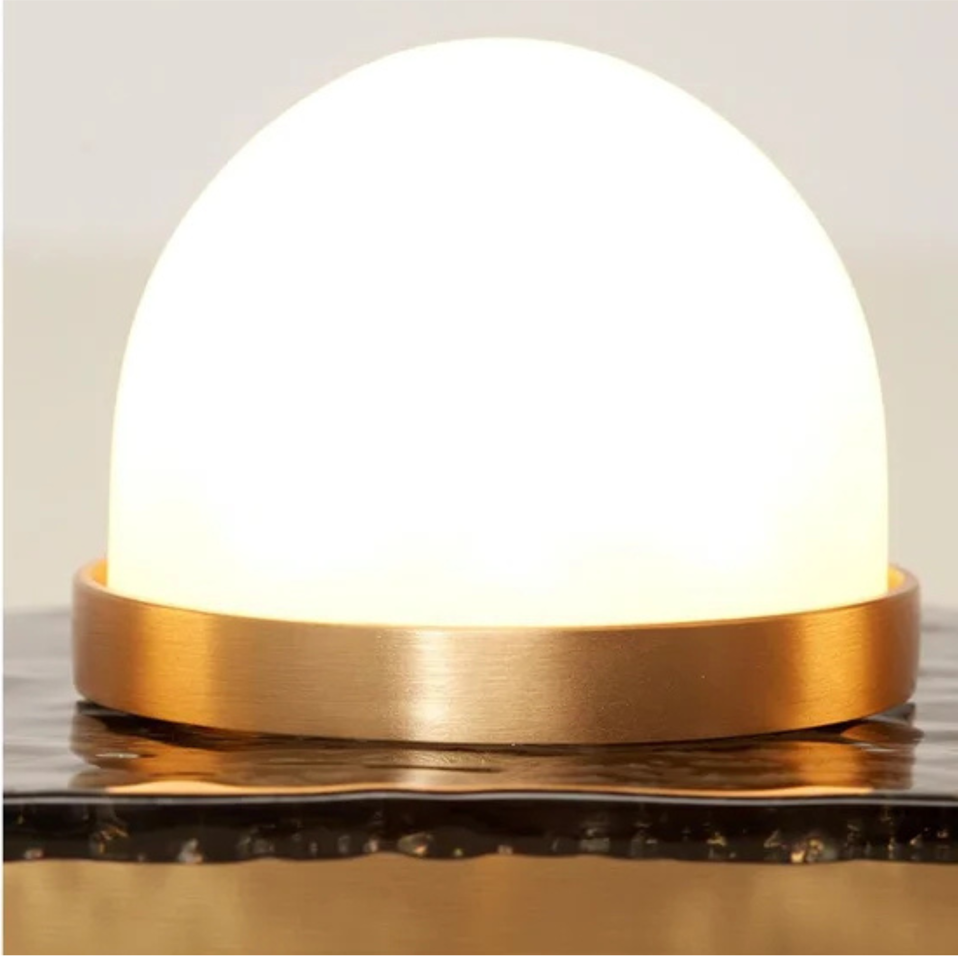 close up of single dome bulb in brushed brass ring on textured metal plate