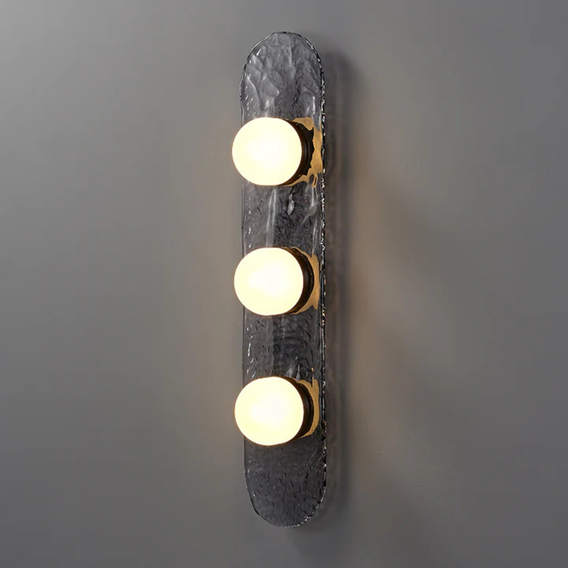 three bulb sconce with brass mount on dark raindrop textured backplate