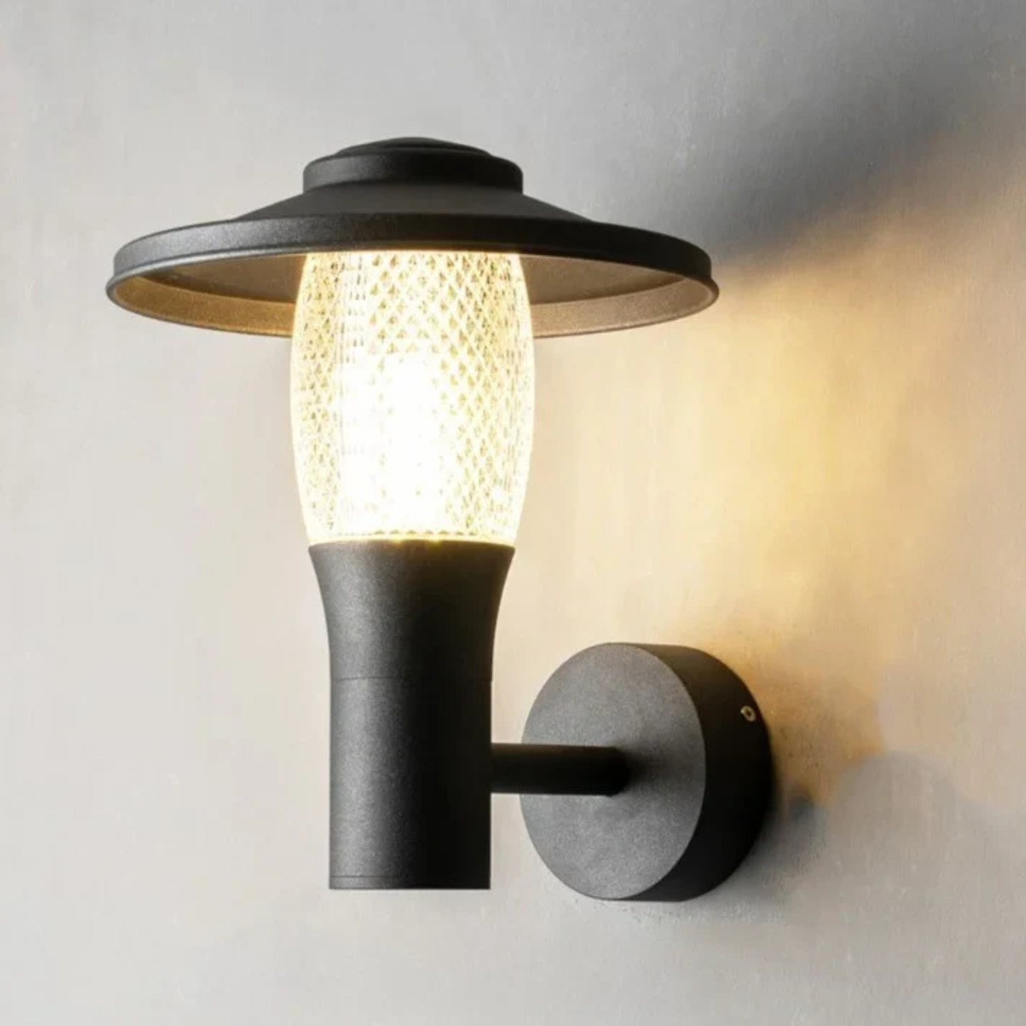 Close-up of sleek black and glass outdoor wall lamp casting warm ambient light on a wall