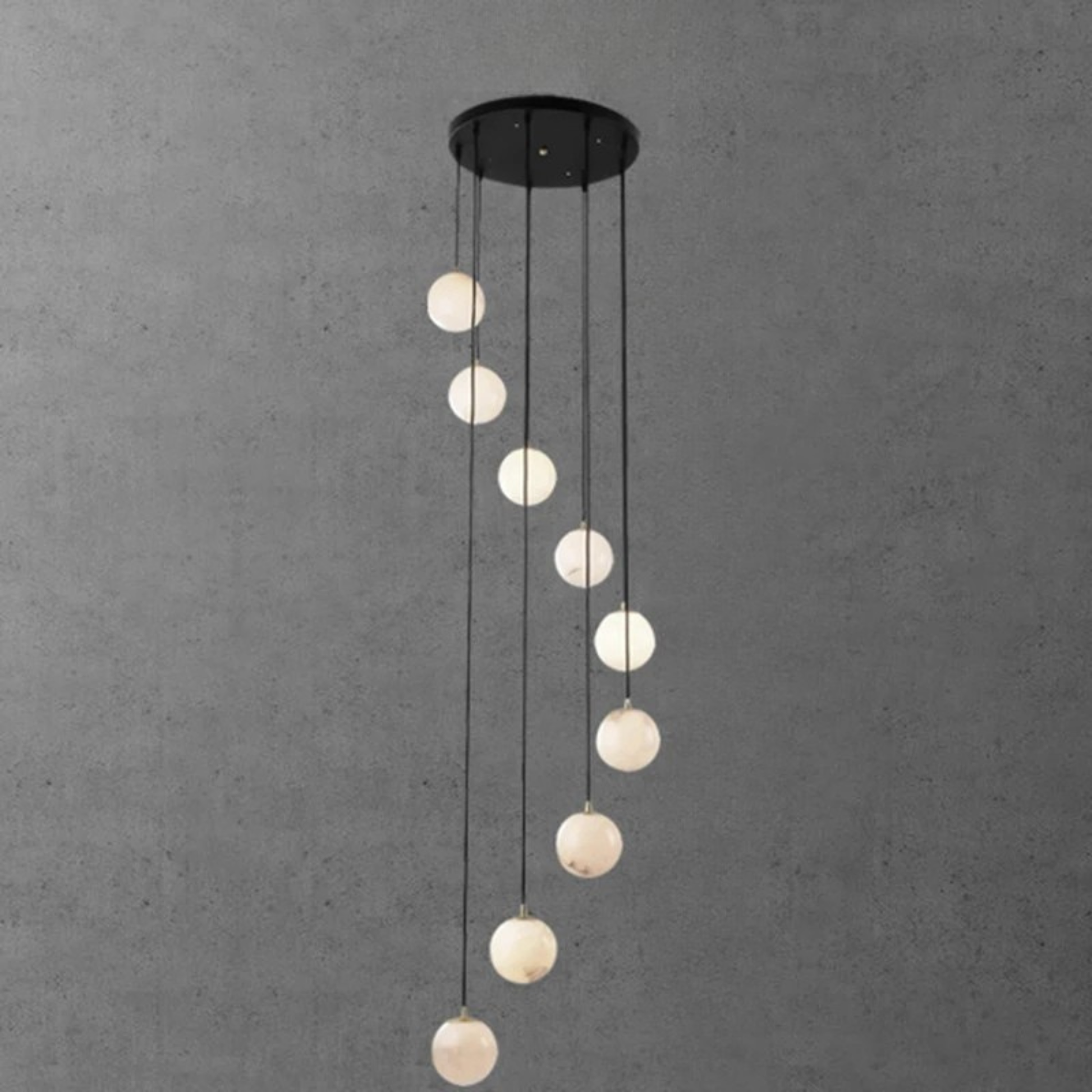 A vertical pendant light installation with white glowing orbs hanging in a wave-like shape against a gray wall.
