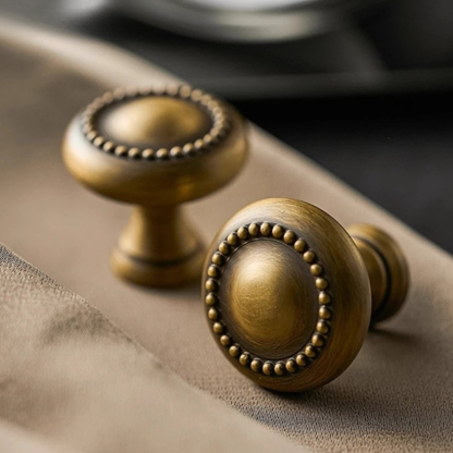 A pair of golden drawer knobs placed on a marble countertop with soft lighting.