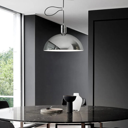 A shiny chrome dome pendant lamp hanging above a dark marble dining table in a modern interior with dark walls.