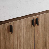 Two modern bronze handles mounted on a light oak cabinet in a minimalist interior.