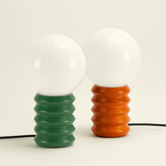 Two light bulbs with ribbed ceramic bases, one green and one orange, on a white background.