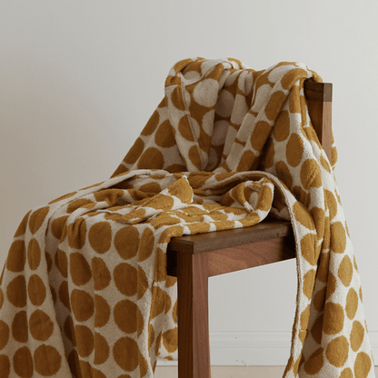 Patterned blanket draped over a wooden chair against a neutral background