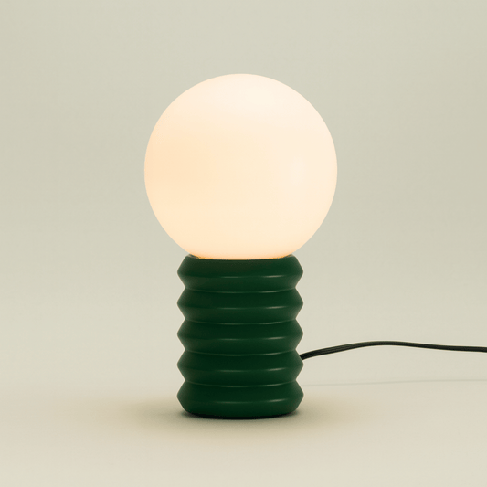 Green textured table lamp with a white bulb on a light beige background