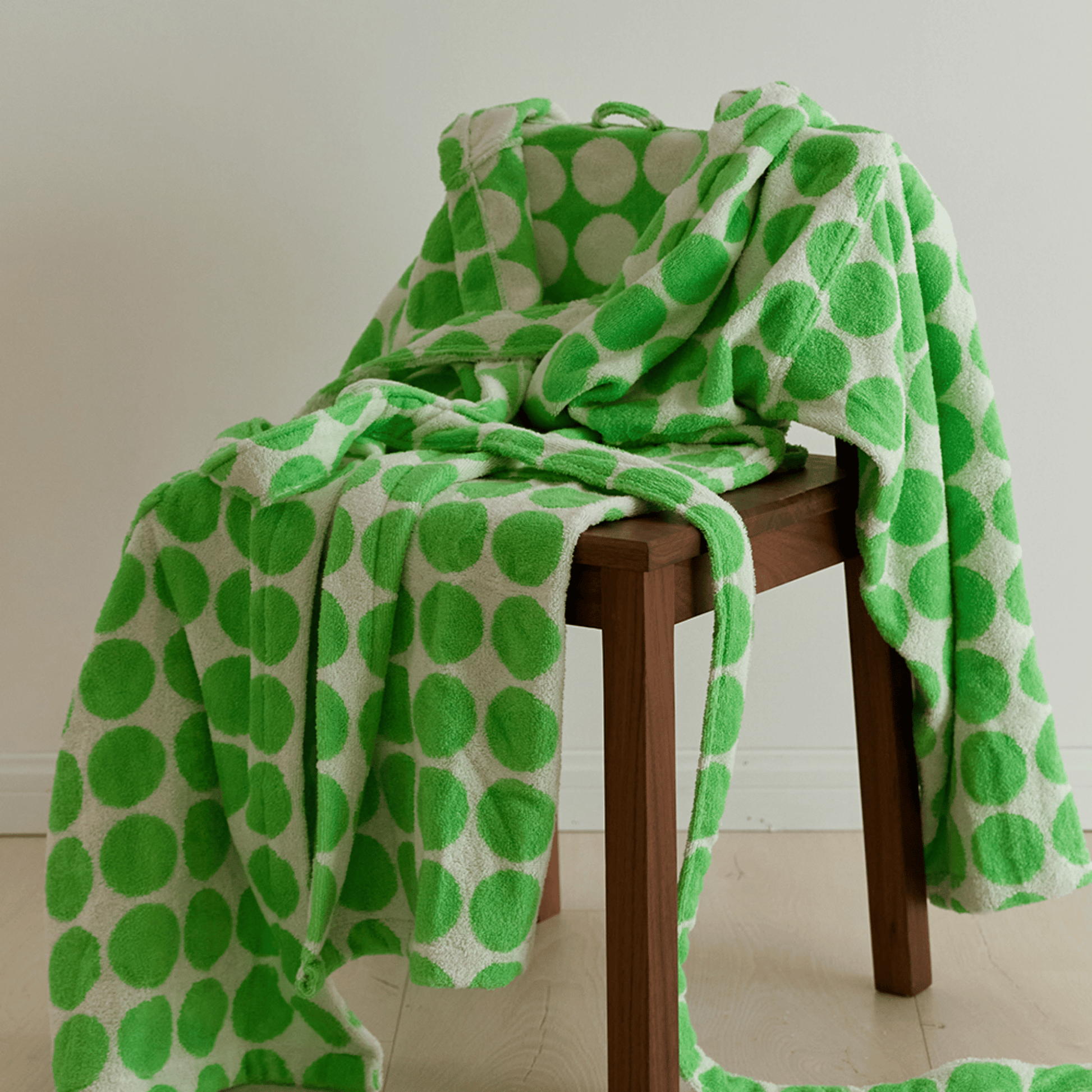 Green and white polka dot towel draped over a wooden stool on a light wooden floor.
