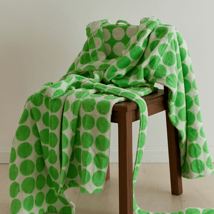 Green and white polka dot towel draped over a wooden stool on a light wooden floor.