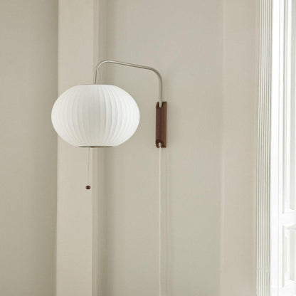 Wall-mounted lamp with a round white shade and wooden base on a beige wall.