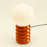 Decorative lamp with a ribbed brown base and white bulb on a beige background