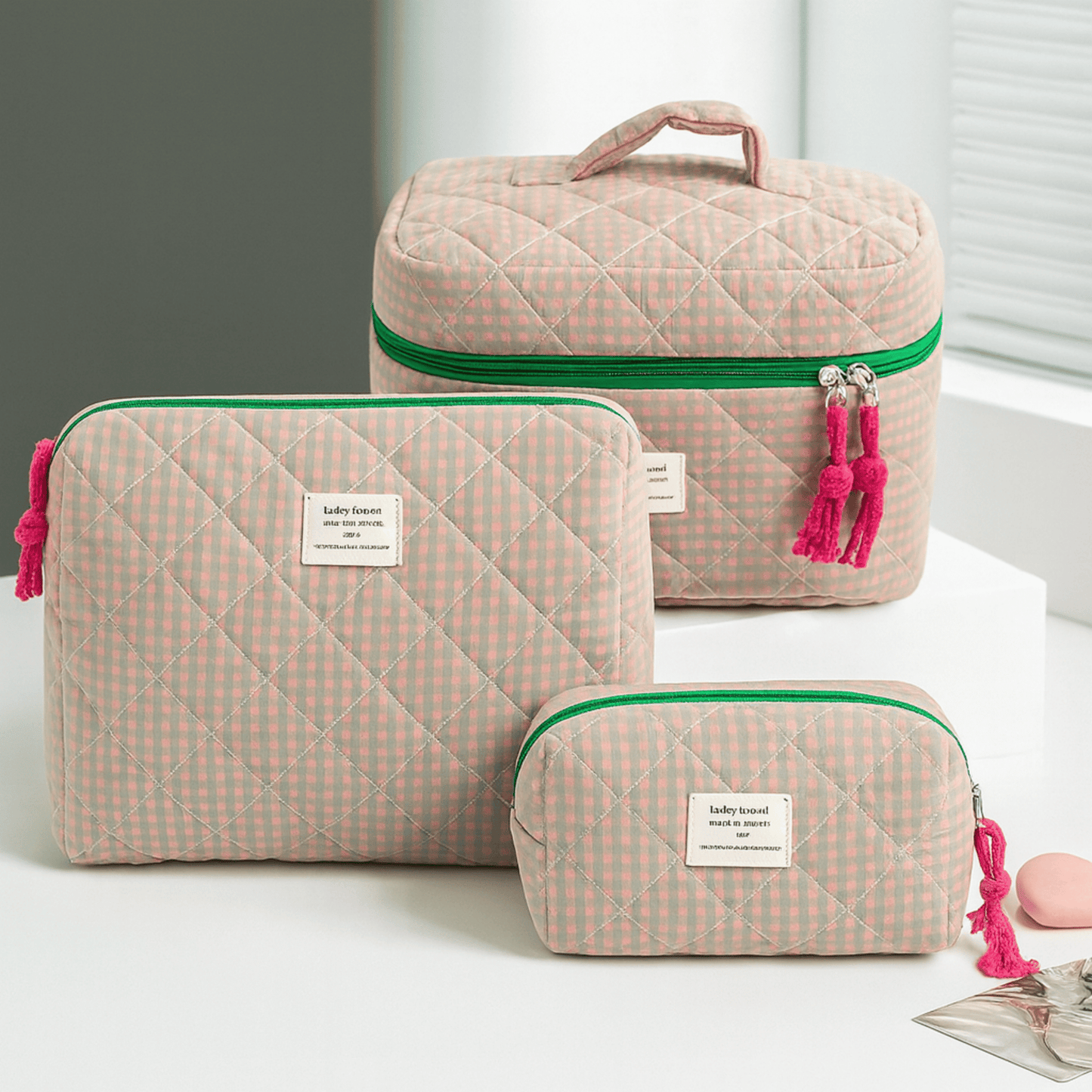 Set of three quilted cosmetic bags with pink and green accents on a light background