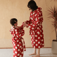 Two people wearing red polka dot robes in a room with a plant.