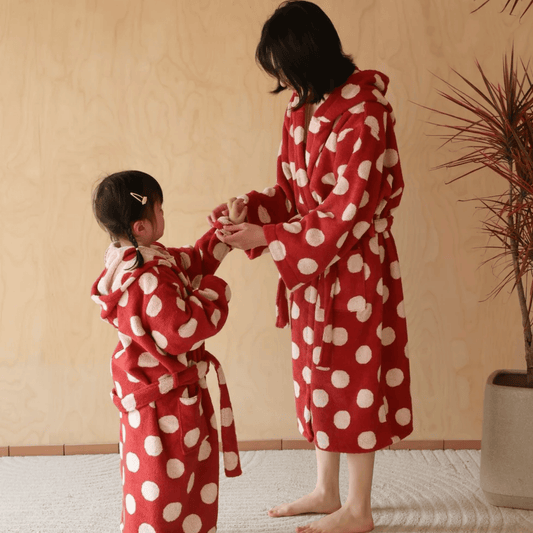 Two people wearing red polka dot robes in a room with a plant.