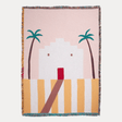 Woven blanket with a design of palm trees and a building on a pink background