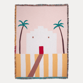 Woven blanket with a design of palm trees and a building on a pink background