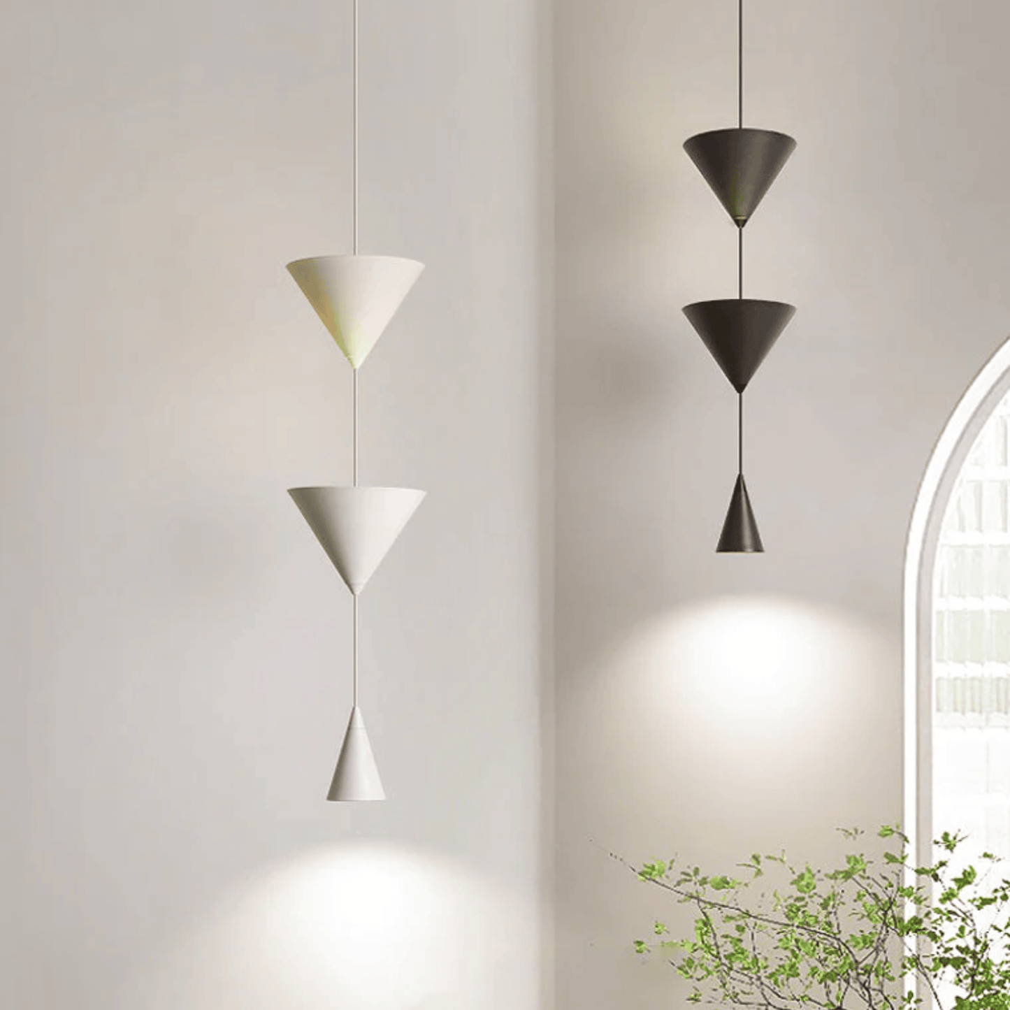 Three modern pendant lights hanging against a neutral wall with a plant in the corner.