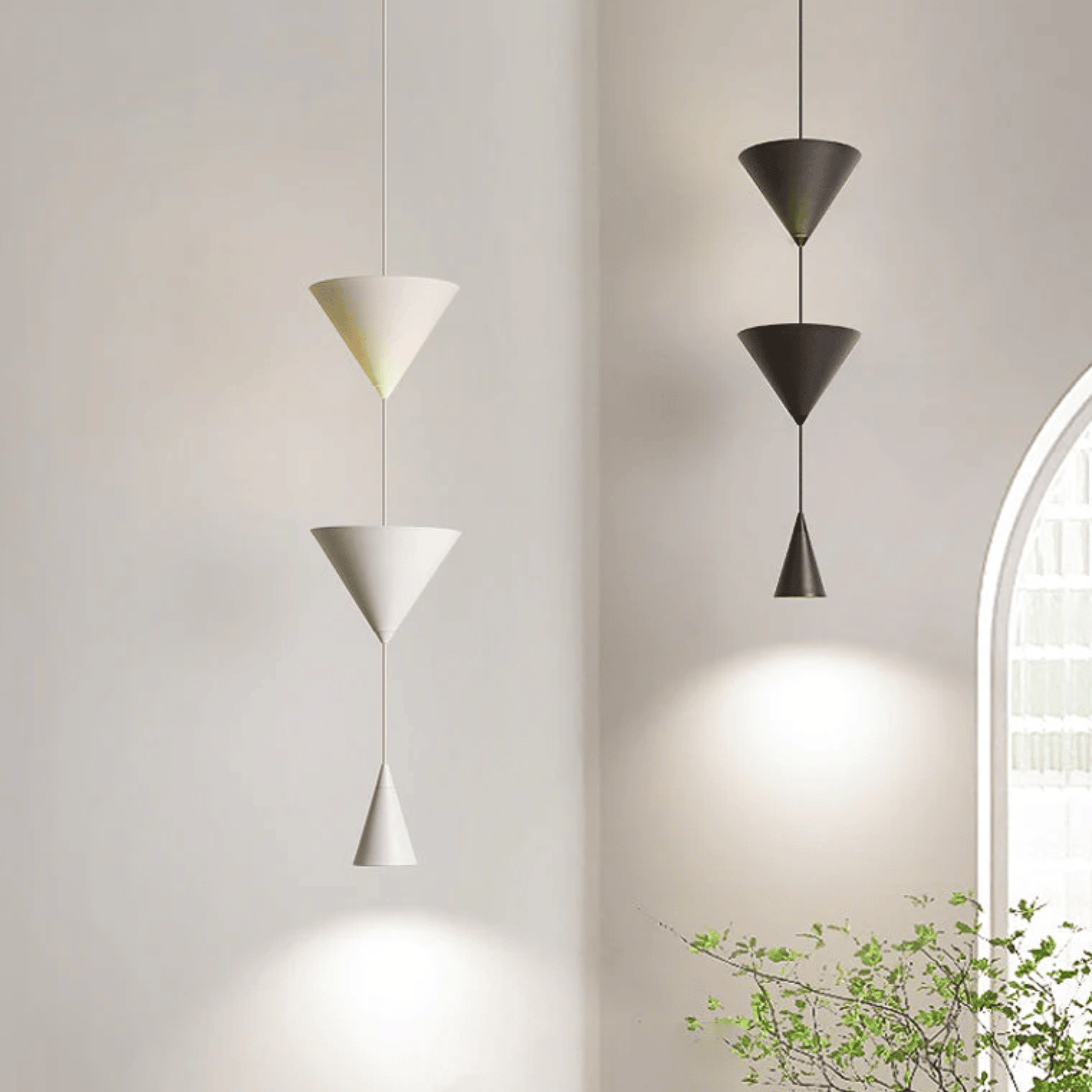 Three modern pendant lights hanging against a neutral wall with a plant in the corner.