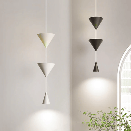 Three modern pendant lights hanging against a neutral wall with a plant in the corner.