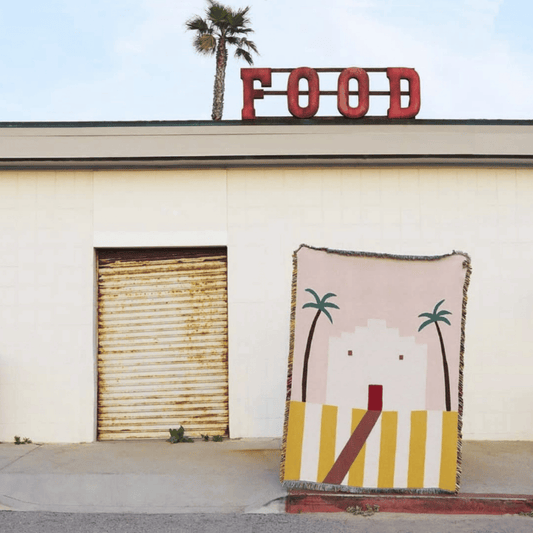 Woven blanket with palm tree design in front of a building with a 'FOOD' sign.