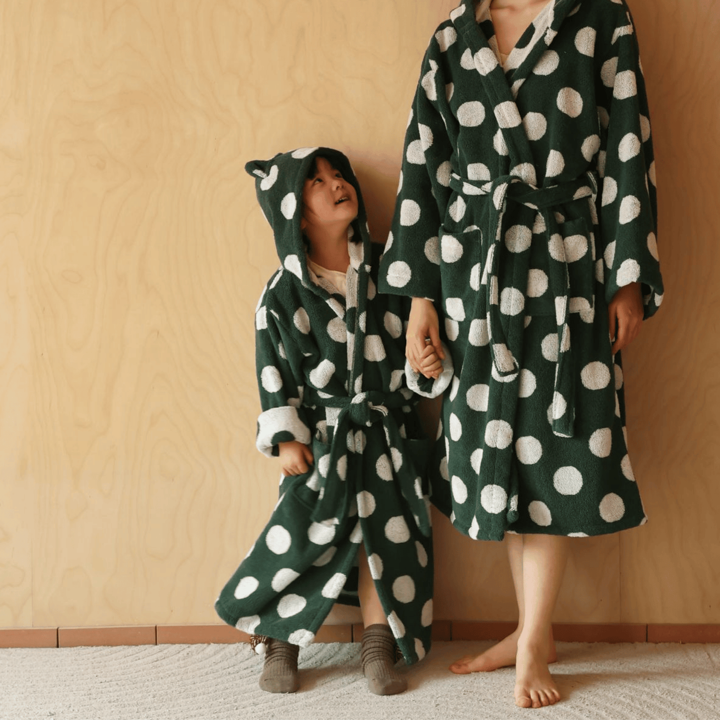 Two people wearing green and white polka dot robes against a beige wall.