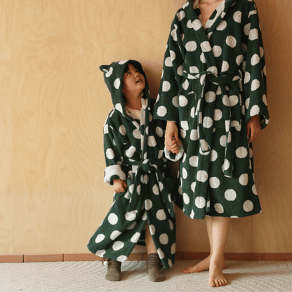 Two people wearing green and white polka dot robes against a beige wall.