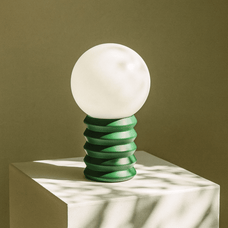 Table lamp with a white globe and green spiral base on a neutral background