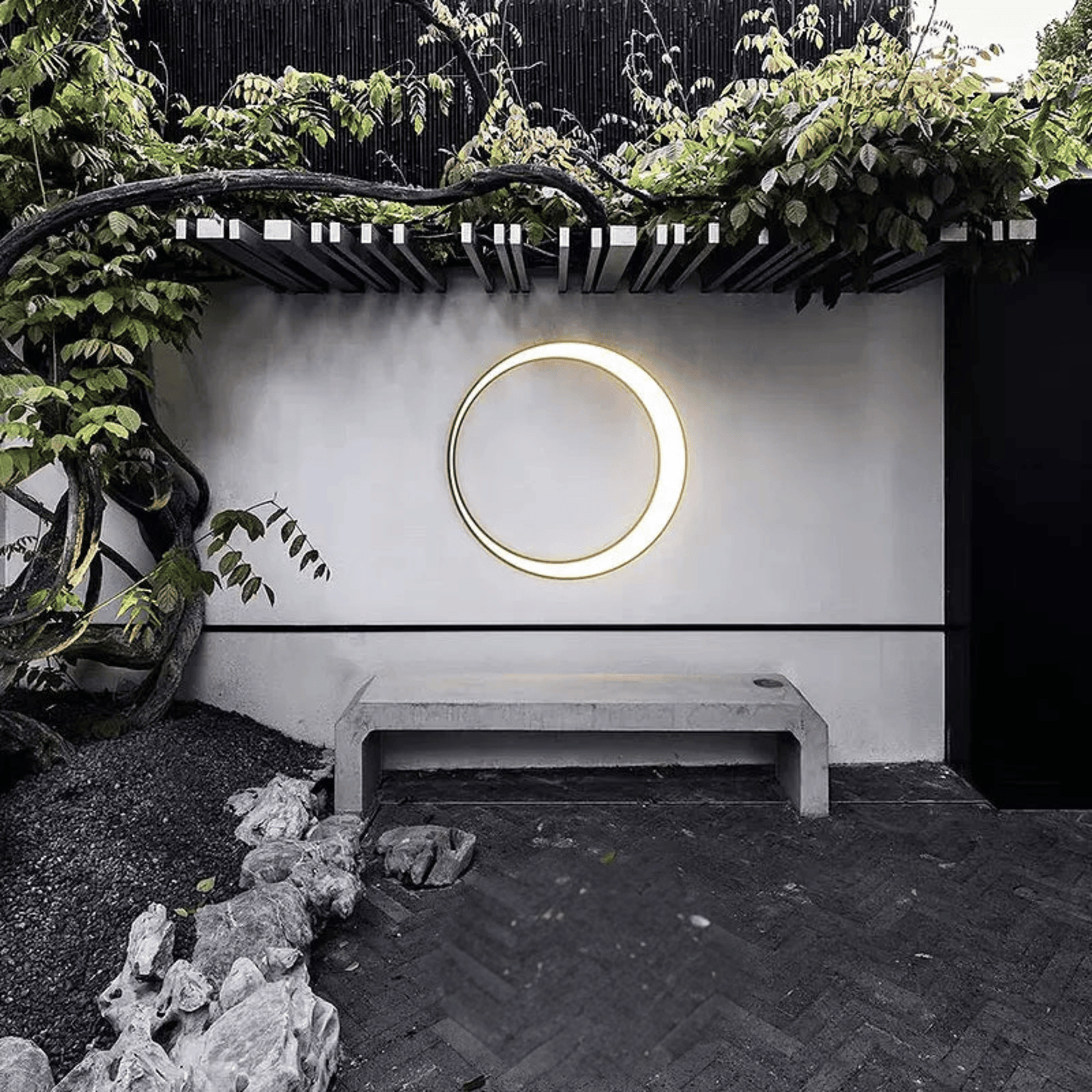Circular light fixture on a white wall with greenery and a bench in the foreground