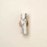 Minimalist marble wall sconce glowing warmly against a light-colored wall.