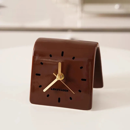 A brown leather desk clock with gold hands and black hour markers placed on a light-colored desk.