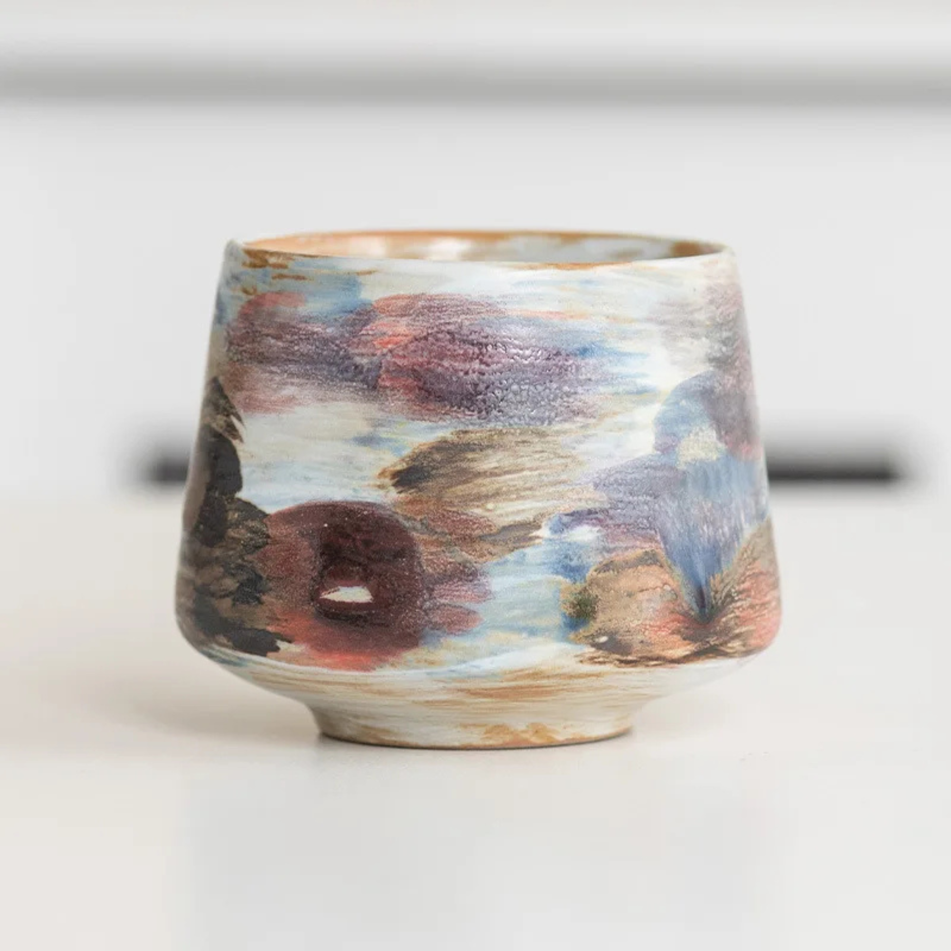 Artisan ceramic cup with a soft blue and pastel watercolor-style glaze.