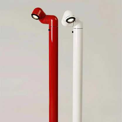 A red and white floor lamp with a sleek design, standing beside a chair and casting light downward.
