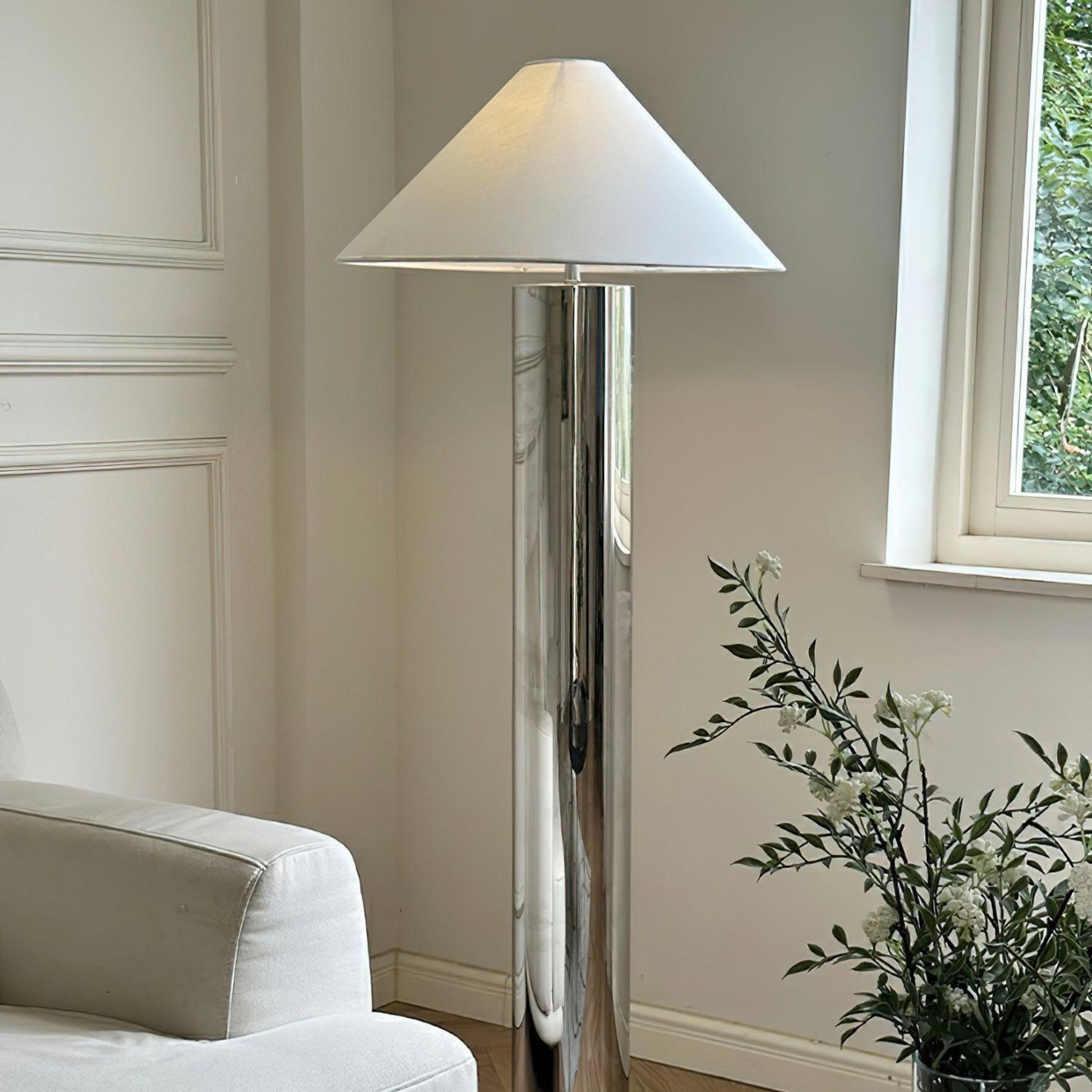 tall chrome floor lamp with a wide cone-shaped white lampshade placed beside a window