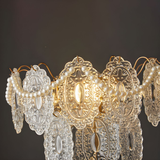 A close-up view of a chandelier-style lamp with intricate crystal details, glowing softly against a dark background.