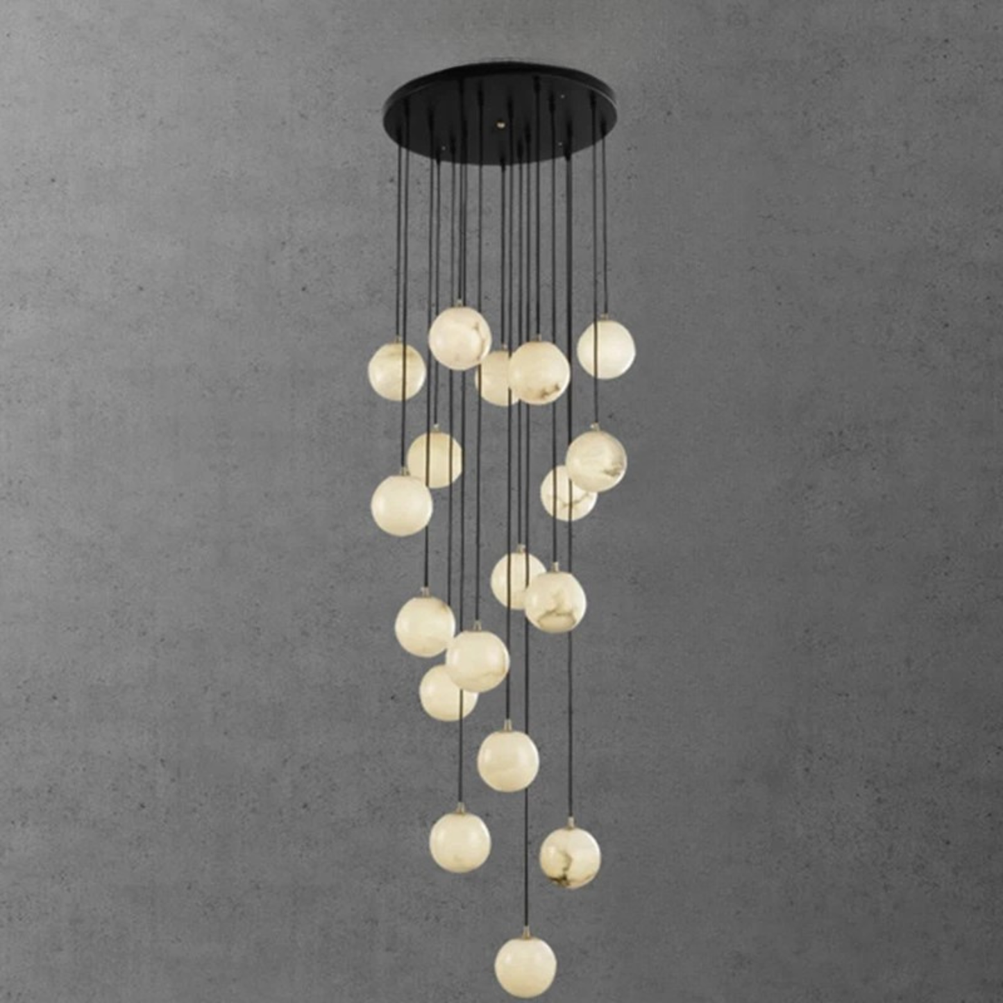 A vertical pendant light installation with white glowing orbs hanging in a wave-like shape against a gray wall.