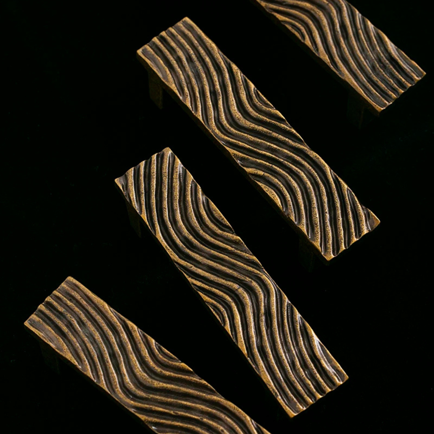 A modern wavy brass handle mounted on a matte black cabinet door, highlighting its detailed texture.