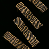 A modern wavy brass handle mounted on a matte black cabinet door, highlighting its detailed texture.