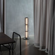 Ribbed-glass floor lamp lighting a modern living space with an orange floor and black furniture.