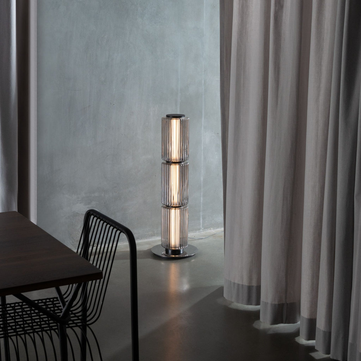 Ribbed-glass floor lamp lighting a modern living space with an orange floor and black furniture.