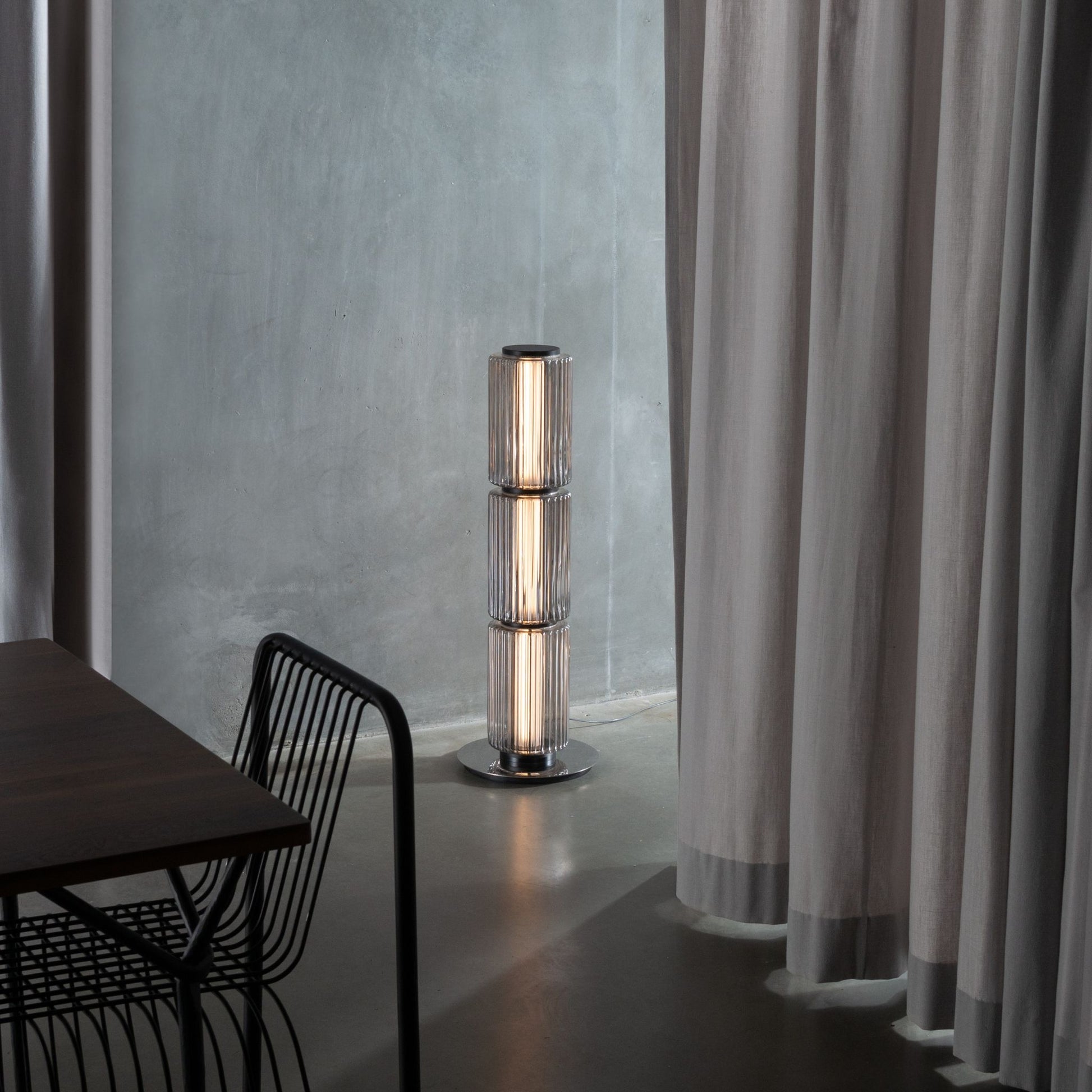 Ribbed-glass floor lamp lighting a modern living space with an orange floor and black furniture.