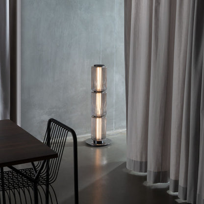 Ribbed-glass floor lamp lighting a modern living space with an orange floor and black furniture.