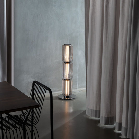 Ribbed-glass floor lamp lighting a modern living space with an orange floor and black furniture.