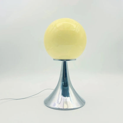 A pale yellow glass globe table lamp on a chrome cone-shaped base displayed on a white surface.