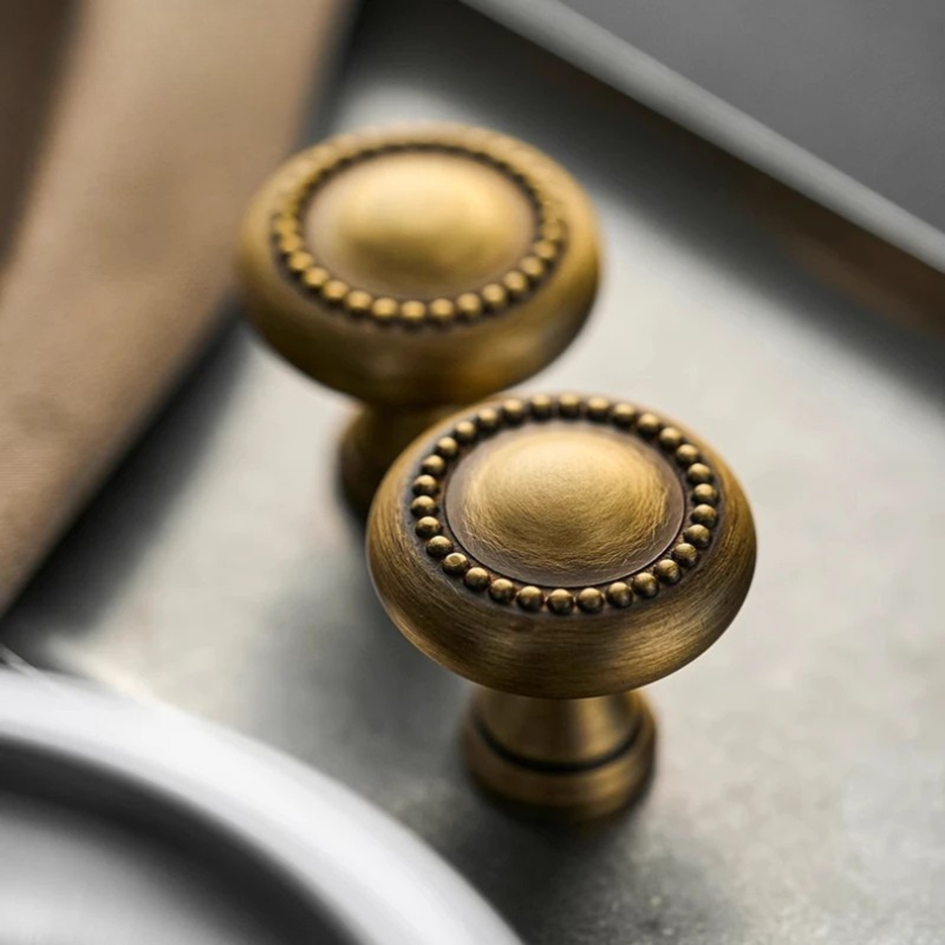 Two antique gold knobs lying side by side on a soft beige fabric background.