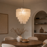 Chandelier hanging above a dining table with a vase and fruit bowl in a room with shelves and a painting.