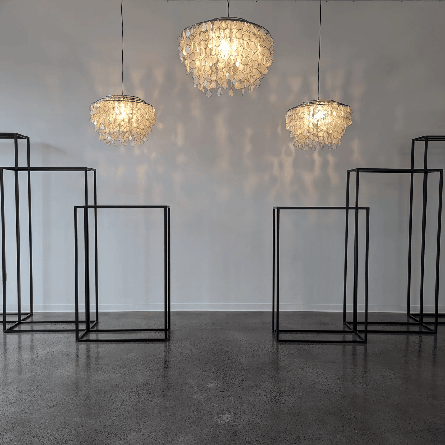Three chandelier-style lamps hanging from the ceiling with black metal stands on a gray floor.