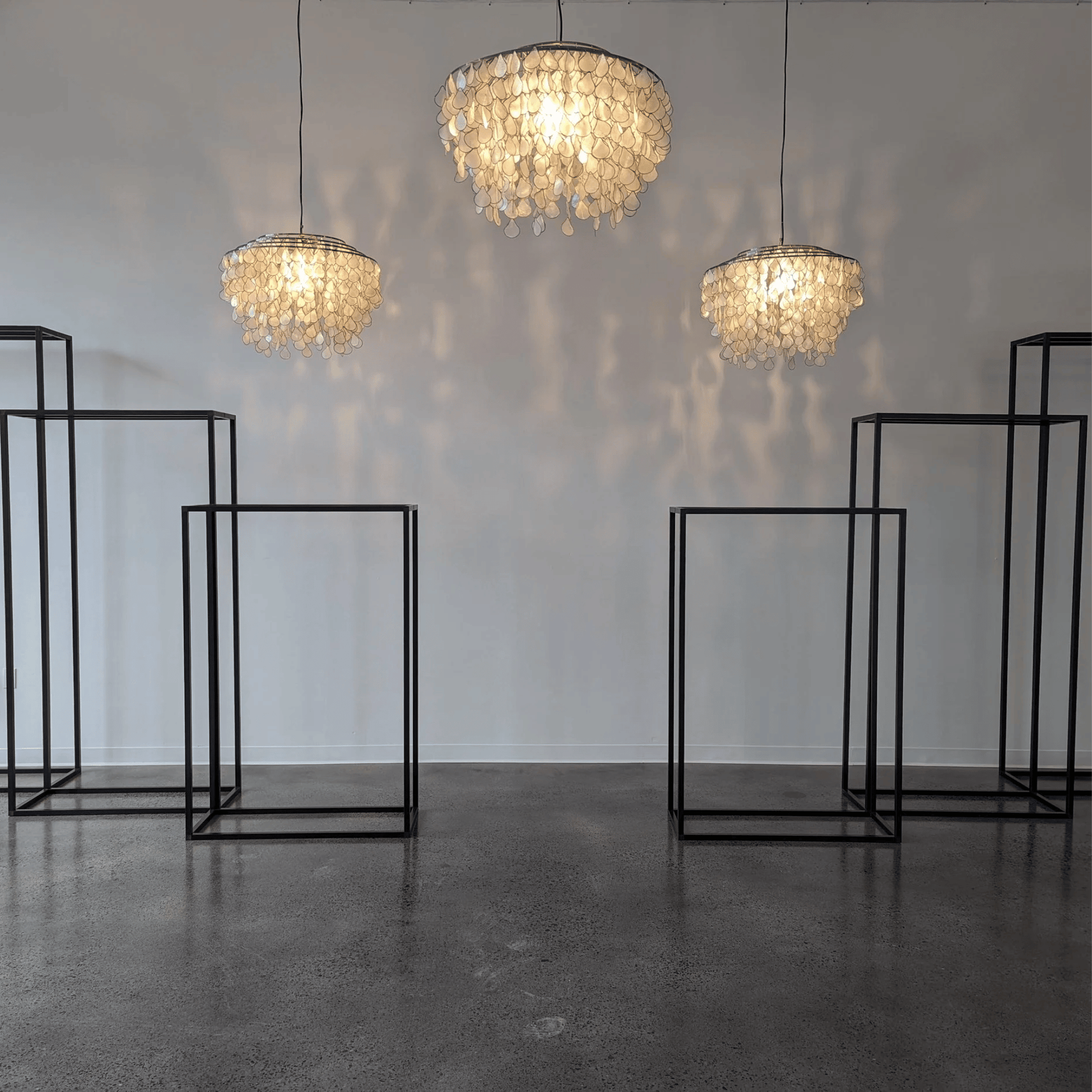 Three chandelier-style lamps hanging from the ceiling with black metal stands on a gray floor.