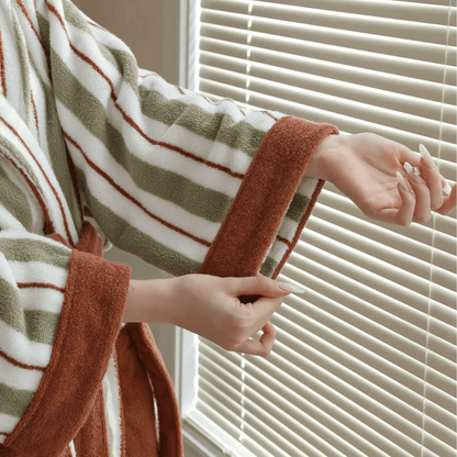 Person wearing a striped robe adjusting blinds in a room.