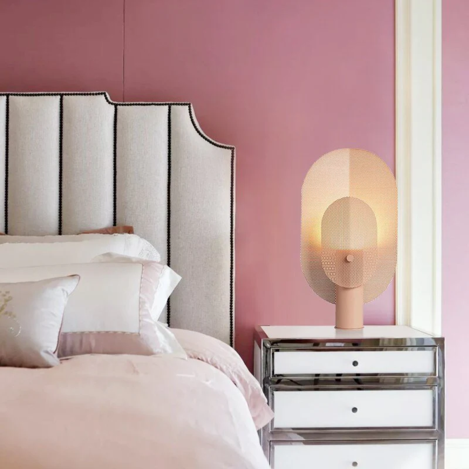 Bedroom with pink walls, a bed with white bedding, and a nightstand with a lamp.